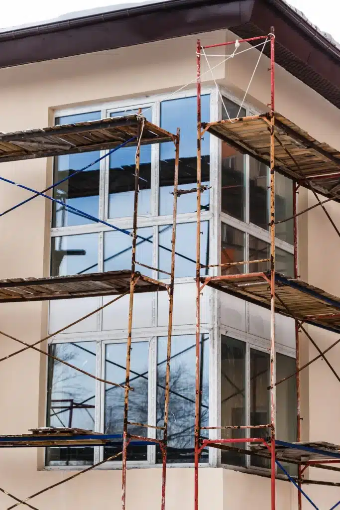 Rénovation façade : échafaudage et pose de fenêtres modernes Échafaudage rouillé devant de grandes baies vitrées d'angle. Façade beige en rénovation avec des fenêtres modernes.